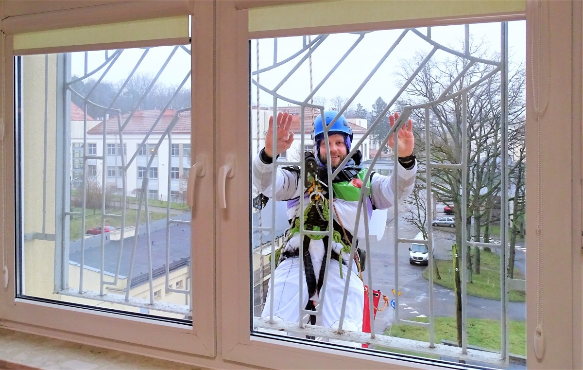 Alpinista zjeżdżający na linie w budynku pozdrawia zza okna małych pacjentów